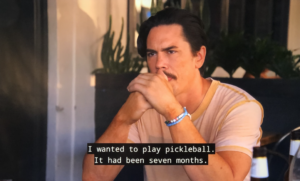 Close up shot of Tom Sandoval, a dark-haired man with a mustache, with his hands clasped in front of his face, with greenery behind his shoulders. A closed caption on the lower half of the image reads: "I wanted to play pickleball. It had been seven months."